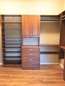 Medium wood tone closet system with adjustable shoe shelving and built in raised panel cabinets with lower drawers and upper doors by Austin-Morgan Closets